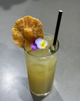 Iced matcha latte with dehydrated pineapple garnish and edible flower in a tall glass