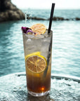 Iced drink with dehydrated lemon slice and edible flowers, served by the ocean on glass table