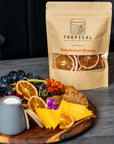 Dehydrated orange slices in retail pouch beside charcuterie board with grapes and cheese.