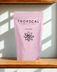Pink pouch of chai powder with star anise design on wooden shelf in sunlight.