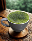 Creamy matcha latte in a white mug on a wooden table by a window, vibrant green foam on top.