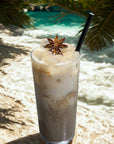 Iced matcha latte with star anise garnish, beach background, luxury tropical drink