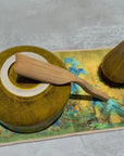Ceramic matcha bowl, bamboo whisk, and wooden matcha spoon on a colorful mat