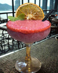 Berry smoothie in a glass garnished with dehydrated orange slice and mint, outdoor setting