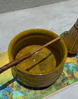 Ceramic matcha bowl, bamboo whisk, and scoop with matcha powder on colorful mat